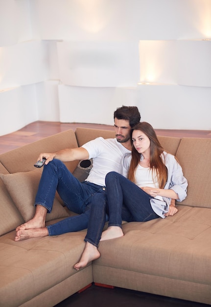 Relaxed young couple watching tv at home in bright living room