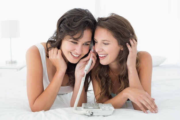 Relaxed young female friends using phone in bed