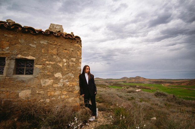Relaxed young girl leaning against an abandoned house in a barren landscape