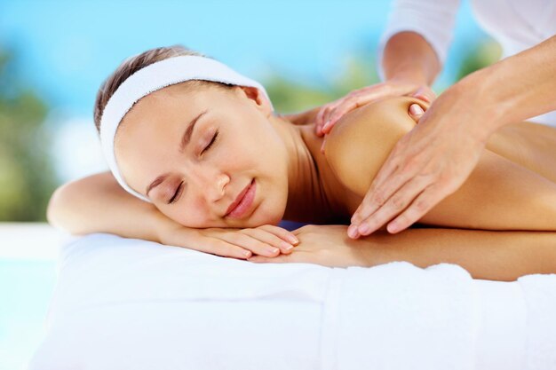 Relaxed young lady receiving shoulder massage from a masseuse Relaxed young woman receiving shoulder massage from a professional masseuse