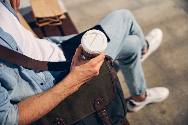 Photo relaxed young man having rest after work and reading news online, going to drink tasty coffee