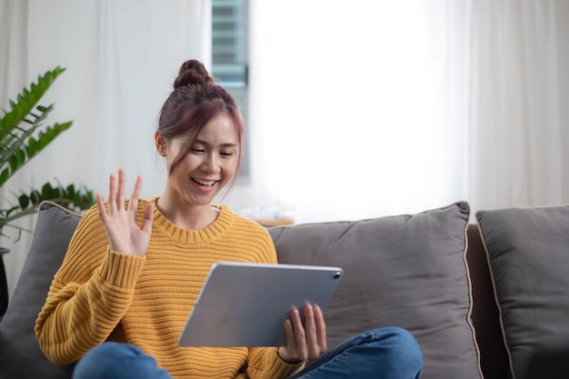 Photo relaxed young mixed race woman in sofa smiling content happy and reading on tablet pc at home in couch lifestyle image of beautiful mixed asian girl relaxing smiling happy