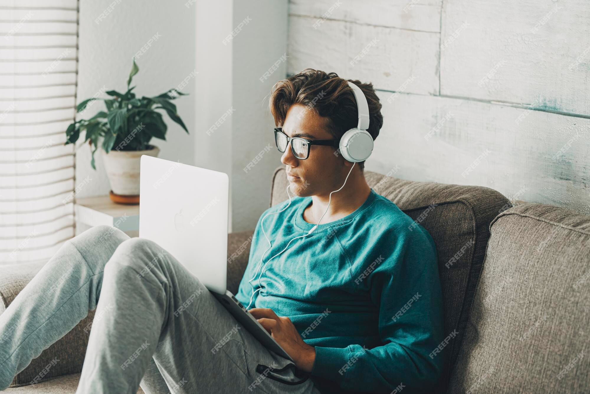 lazy teenager boy play computer games, sit in headphones, looking at screen  of laptop, free time at home Stock Photo