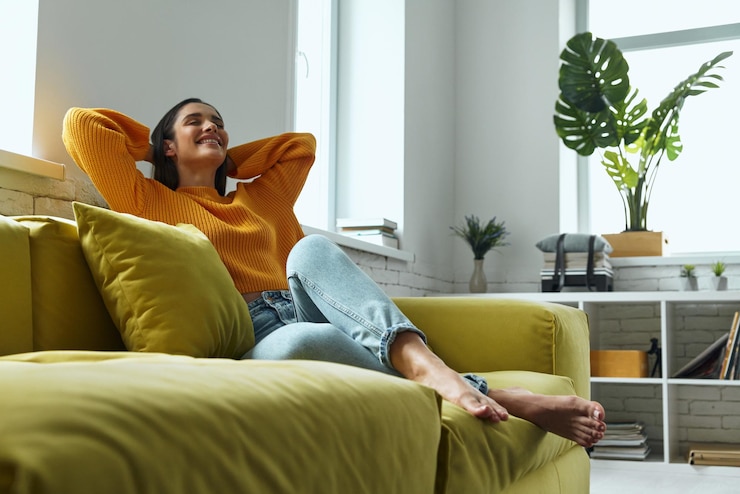 Photo relaxed young woman holding hands behind head while sitting on the couch at home