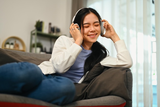 Relaxed young woman listening music on headphones with closed eyes enjoying music