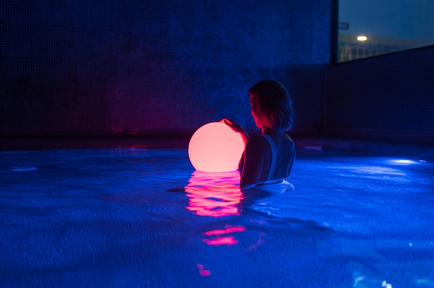 Relaxed young woman in pool with neon light