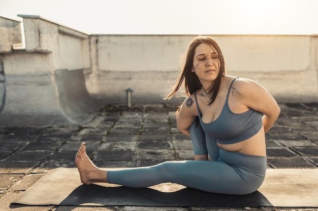 Relaxed young woman practicing yoga stretching exercise on a rooftop terrace.