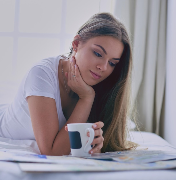 Foto giovane donna rilassata seduta sul letto con una tazza di caffè e un tablet digitale