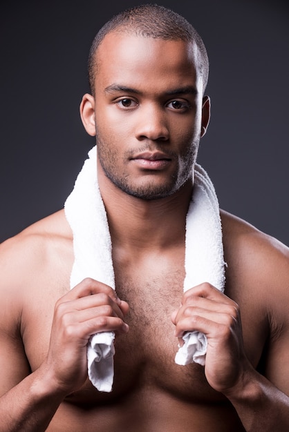 Relaxing after training. Young shirtless African man carrying towel on shoulders