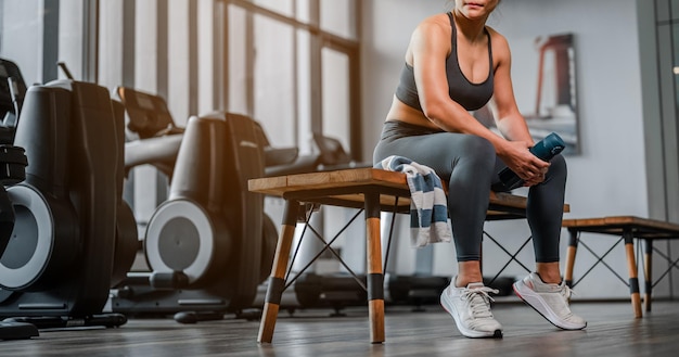 Foto rilassarsi dopo l'allenamentodonna asiatica che distoglie lo sguardo mentre è seduta in palestradonna in palestra che si prende una pausa dall'allenamento e beve proteine modo di allenarsi e concetti di stile di vita fitness