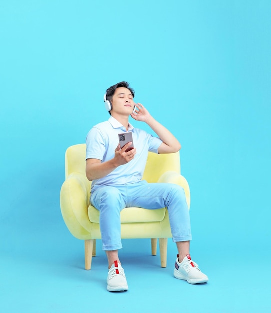 Relaxing Asian young handsome guy sit on single sofa use smart phone isolated on background