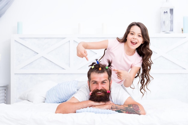 Relaxing in bedroom Affection and support Stay home and have fun Family leisure concept Girl making hairdo for dad Quarantine with children Happy family Pajamas party Happy childhood