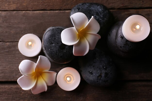 Relaxing composition with exotic fragipani flower, pebbles and candles on wooden wall