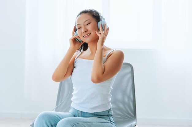 Relaxing dancing cheerful tanned lovely young asian woman in
headphones moves to music at home interior living room sound studio
stream social media concept cool offer banner wide angle