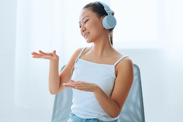 Relaxing dancing cheerful tanned lovely young asian woman in\
headphones moves to music at home interior living room sound studio\
stream social media concept cool offer banner wide angle