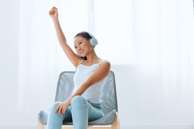 Relaxing dancing cheerful tanned lovely young asian woman in
headphones moves to music at home interior living room sound studio
stream social media concept cool offer banner wide angle