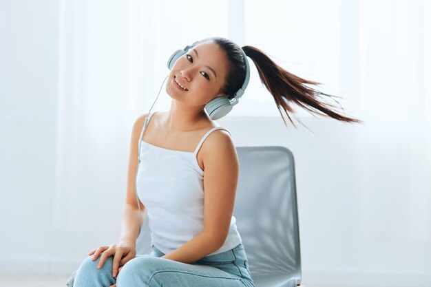 Relaxing dancing cheerful tanned lovely young asian woman in\
headphones moves to music at home interior living room sound studio\
stream social media concept cool offer banner wide angle