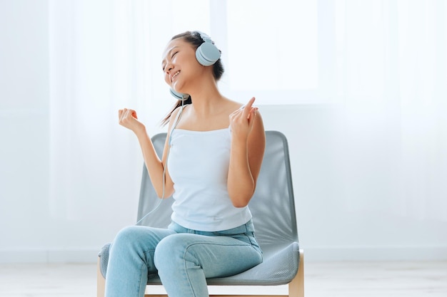 Relaxing dancing cheerful tanned lovely young asian woman in\
headphones moves to music at home interior living room sound studio\
stream social media concept cool offer banner wide angle