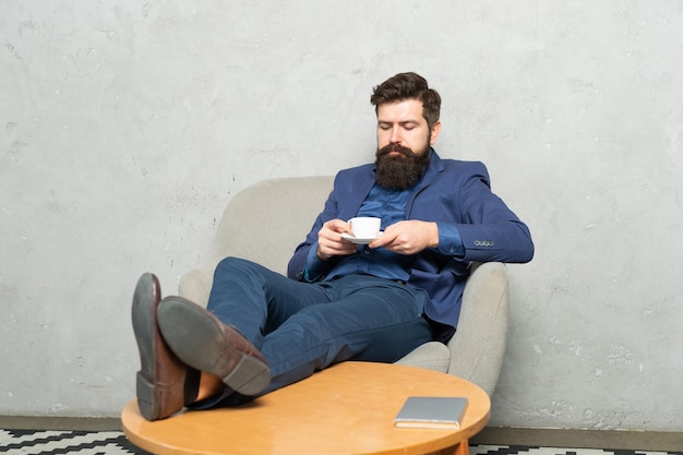 Relaxing guy employee drink tea sitting feet up in rest armchair, tea break.