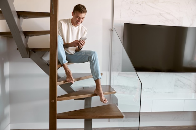 Foto rilassante uomo caucasico felice sulle scale minimaliste in un moderno appartamento luminoso