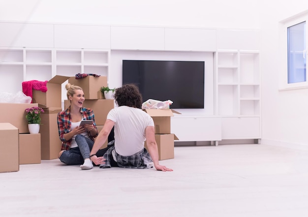 Relaxing in new house. Cheerful young couple sitting on the floor while cardboard boxes laying all around them