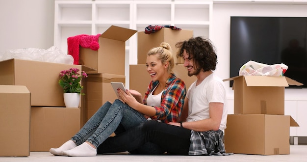 Relaxing in new house. Cheerful young couple sitting on the floor while cardboard boxes laying all around them