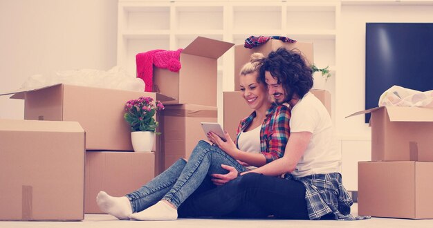 Photo relaxing in new house. cheerful young couple sitting on the floor while cardboard boxes laying all around them