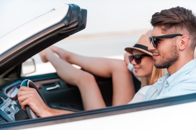 Relaxing during road trip. Beautiful young couple smiling and looking forward while riding in their white convertible