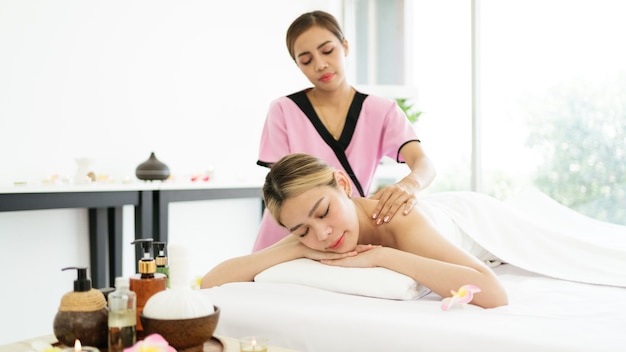 Расслабляющая молодая азиатская женщина лежит и закрывает глаза на массажных кроватях, получая массаж от терапевта в азиатском роскошном спа-салоне и оздоровительном центре в ожидании концепции спа-салона