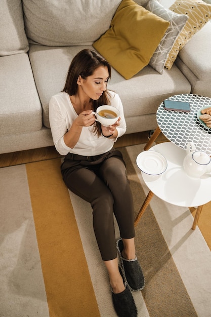 Relaxing young woman sitting on the floor in her living room and enjoy drinking tea at afternoon.