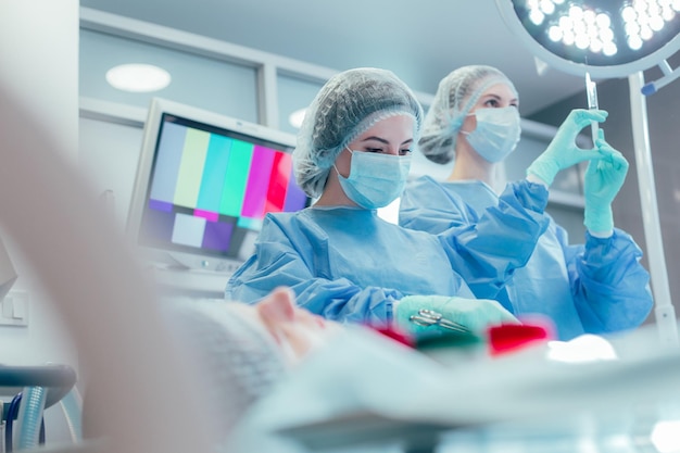 Reliable experienced female doctors standing under the surgical lamp near their patient and operating him