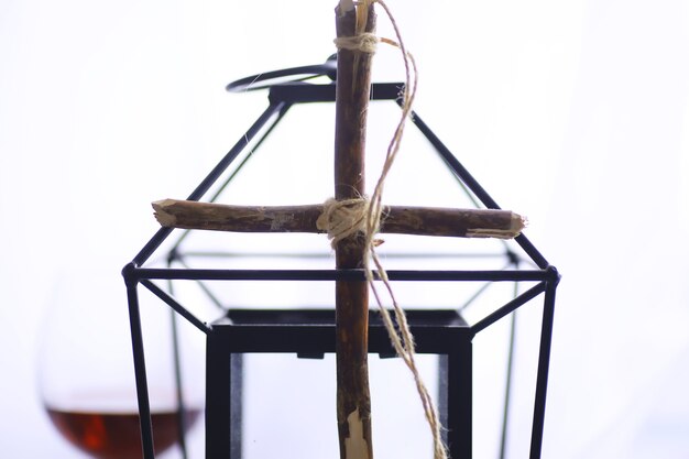 Religieus begrip. met de hand gemaakt houten kruis op een witte achtergrond. wijnglazen lamp met kaarsen.