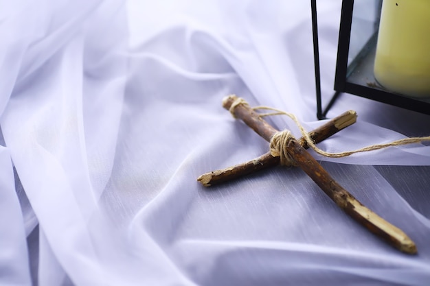 Foto religieus begrip. met de hand gemaakt houten kruis op een witte achtergrond. wijnglazen lamp met kaarsen.