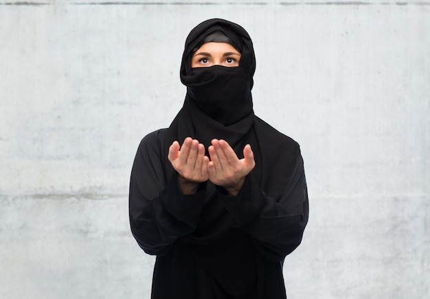 religion, faith, islam and people concept - praying muslim woman in hijab over gray concrete wall background