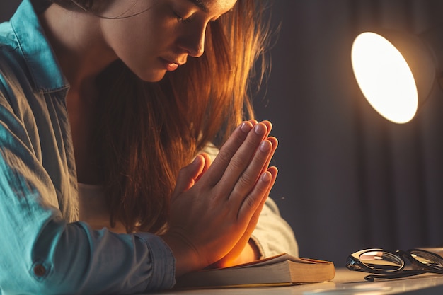 Foto religione donna che prega con la bibbia la sera a casa e si rivolge a dio, chiede perdono e crede nella bontà. vita cristiana e fede in dio