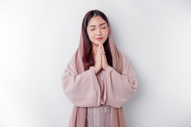 Religious beautiful Asian Muslim girl wearing a headscarf praying to God isolated by white background