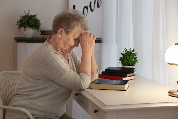 Donna anziana religiosa che prega sopra la bibbia al tavolo