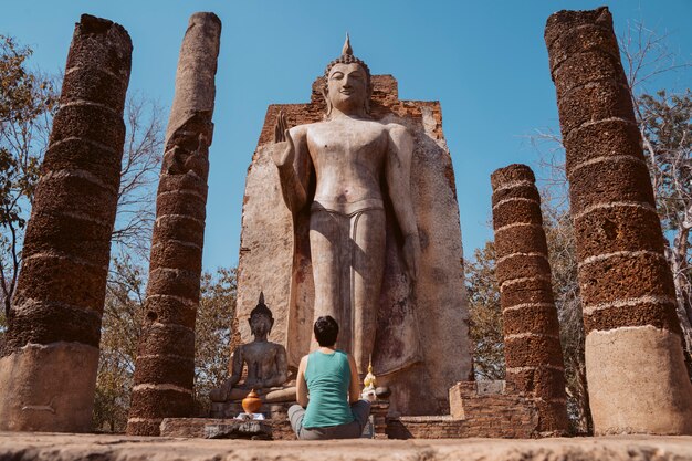 Religious european tourist woman sightseeing the historical temples in Sukhothai. Standing buddha Wat Saphan Hin in Thailand.