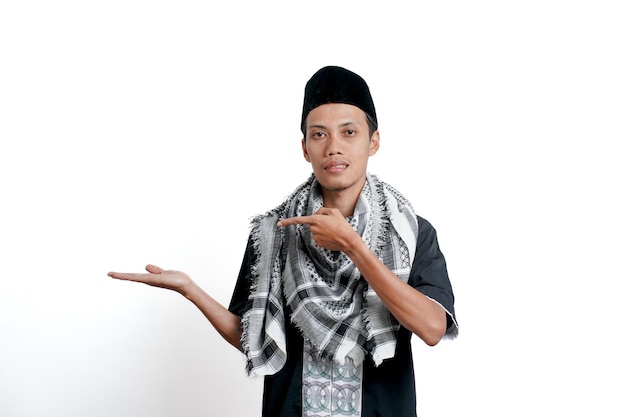 Religious muslim asian man wearing turban muslim dress and cap pointing to the side of empty space Isolated on white background