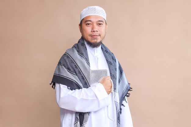 Religious muslim man holding Quran in front of his chest over beige background