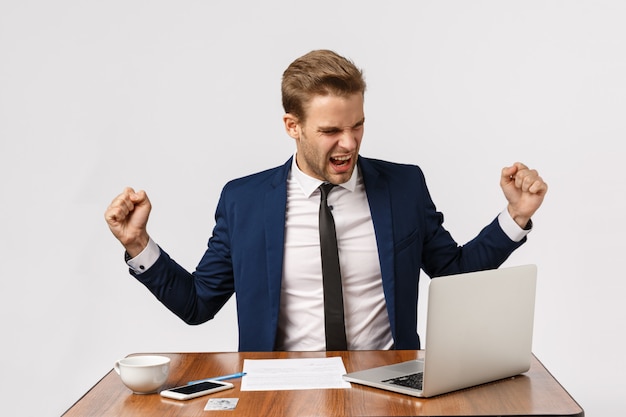 Concetto di gusto, successo e celebrazione. allegro capo di bell'aspetto, che celebra una buona notizia, fa ballare il campione agitando le mani compiaciuto, trionfando, guardando laptop sorridente, offerta vincente