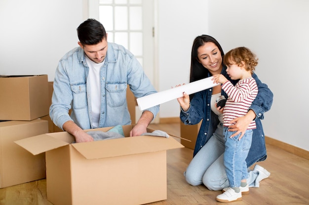 Relocation day concept cheerful family of three unpacking belongings at new home