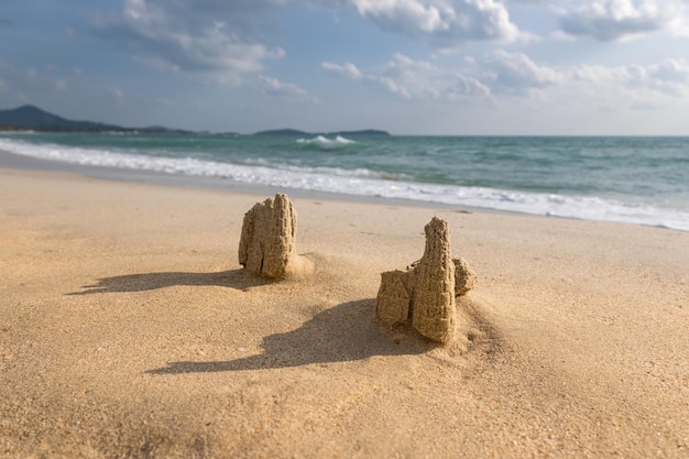 Remains of sand castle on sandy beach in sunlight with mountains in background Koh Samui Thailand