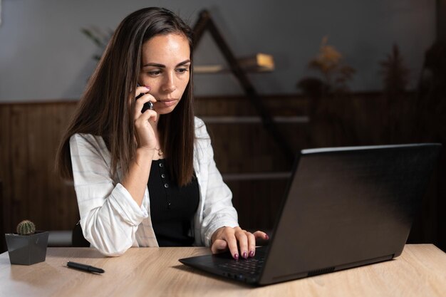 Il libero professionista remoto o la donna d'affari che ha una telefonata utilizza un laptop in ufficio oa casa seduto a un tavolo gadget concettuali di tecnologia online e delle telecomunicazioni per il lavoro