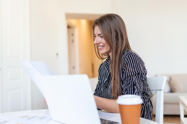 Remote job technology and people concept happy smiling young\
business woman with laptop computer and papers working at home\
office during the covid19 health crisis