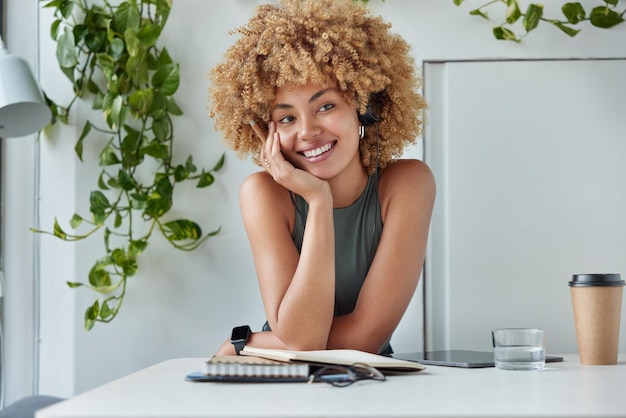 Remote learning diligent female student prepares for exam\
writes up notes thesis for research report essay listens audio\
track via headphones sits at desktop with notebooks tablet coffee\
around