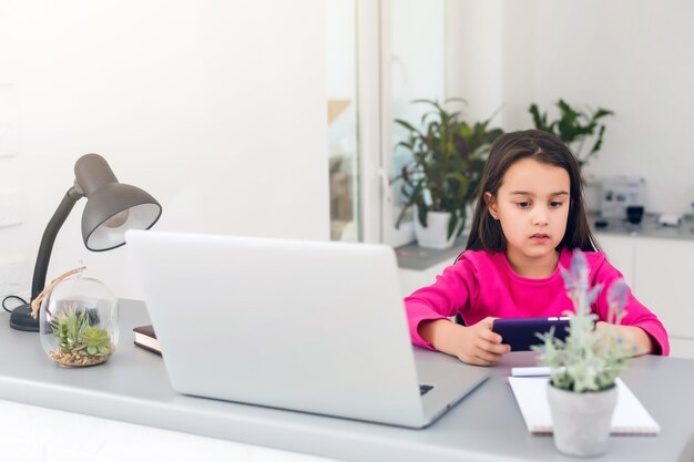 Lezioni a distanza. il bambino sorride felice e acquisisce conoscenza a distanza. la bambina studia l'apprendimento online da casa con il computer portatile. scuola in linea.