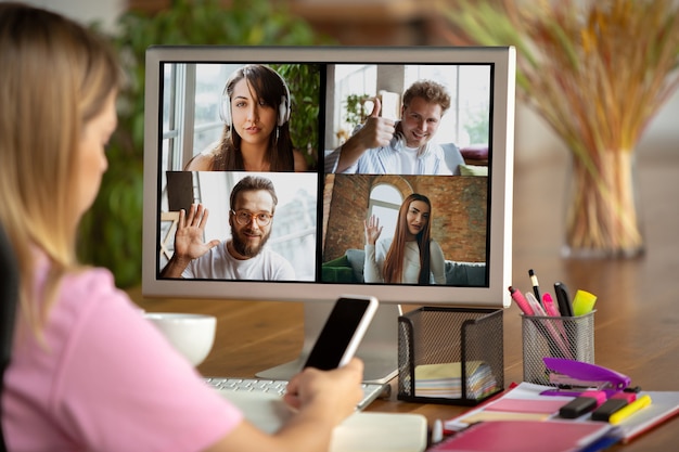 Remote meeting. Woman working from home during coronavirus or COVID-19 quarantine, remote office concept. Young boss, manager in front of monitor during online conference with colleagues and team.