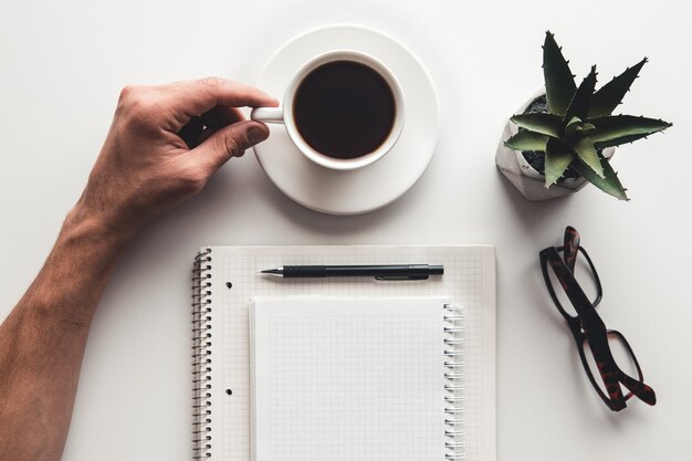 Luogo di lavoro remoto con mano di uomini, tastiera, tazza di caffè e blocco note.