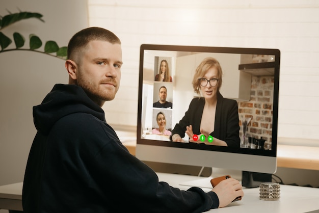 Lavoro a distanza. una vista posteriore di un uomo durante una videochiamata con i suoi colleghi sul computer desktop. un ragazzo distratto da un briefing online a casa.